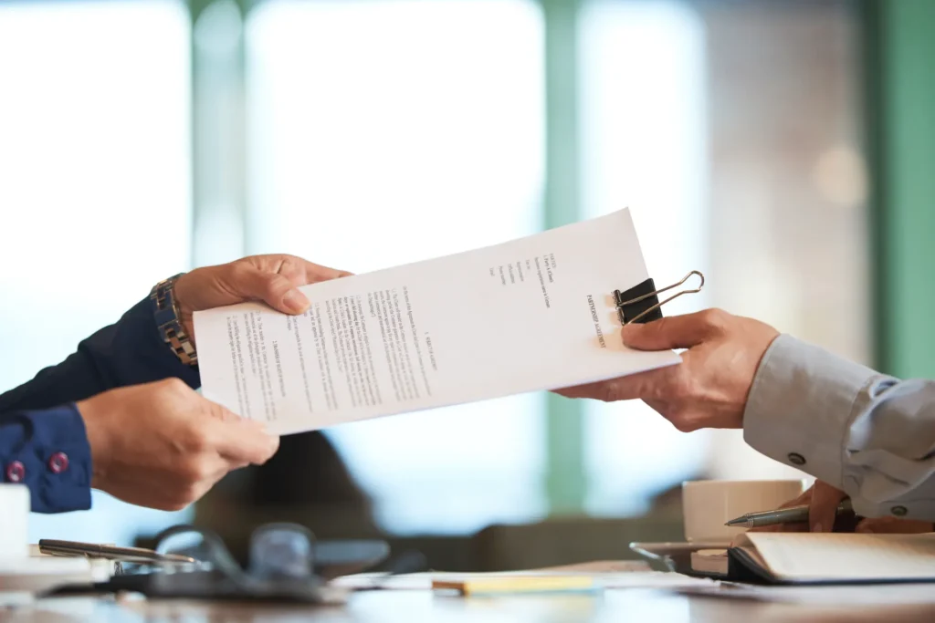 Pessoas em um escritório assinam um documento com segurança, segurando o papel entre mãos. Vem como contexto para seguro garantia e formalização de contrato.